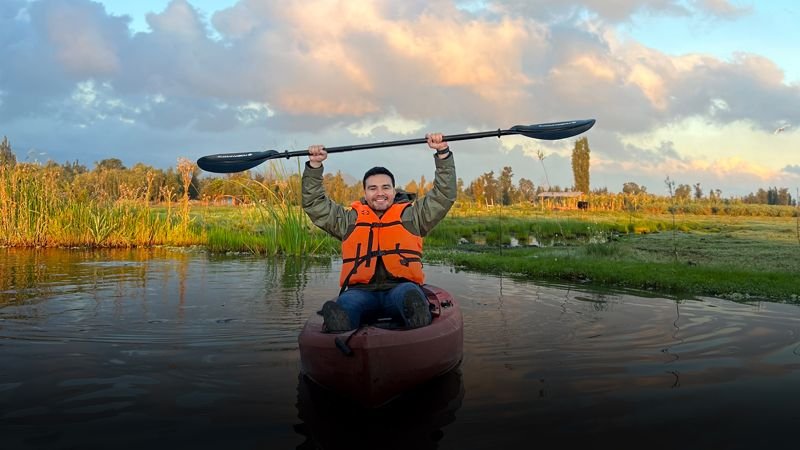 Remero levantando su pala en kayak entre la vegetación de las chinampas