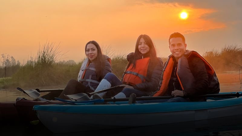 Tres personas sonrientes en kayak al atardecer en Xochimilco