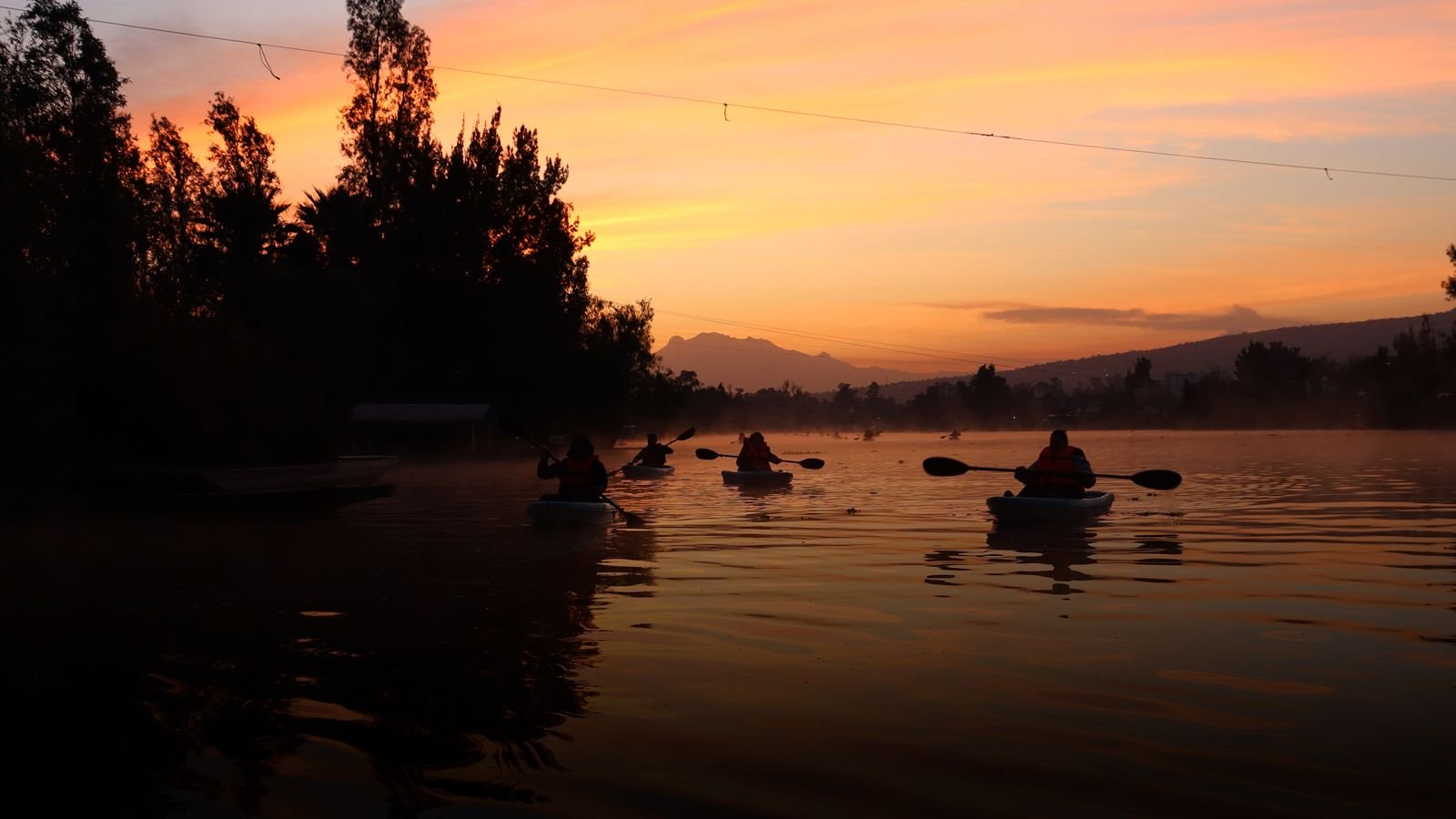 Kayaks en silueta sobre los canales de Xochimilco con el cielo naranja